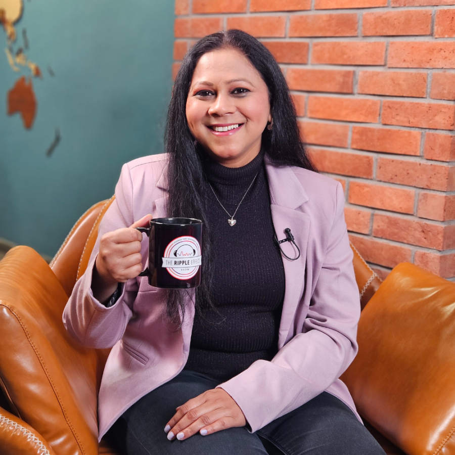 Archana Chauhan holding a mug with 'therippleeffect.show' printed on it, seated on the guest chair of The Ripple Effect show